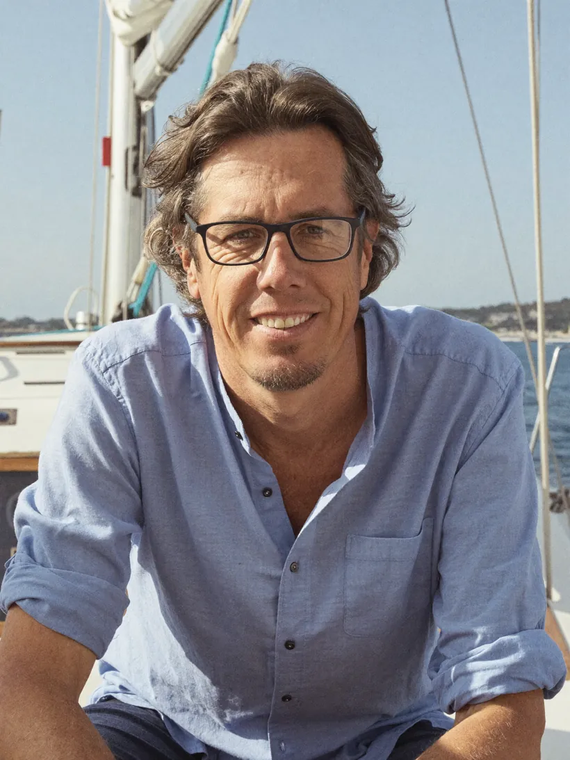 Christian Steinscherer arbeitet mit dem Laptop am Wasser, im Hintergrund ein Boot